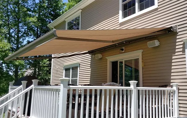Tan retractable awning extended over a deck attached to a beige house