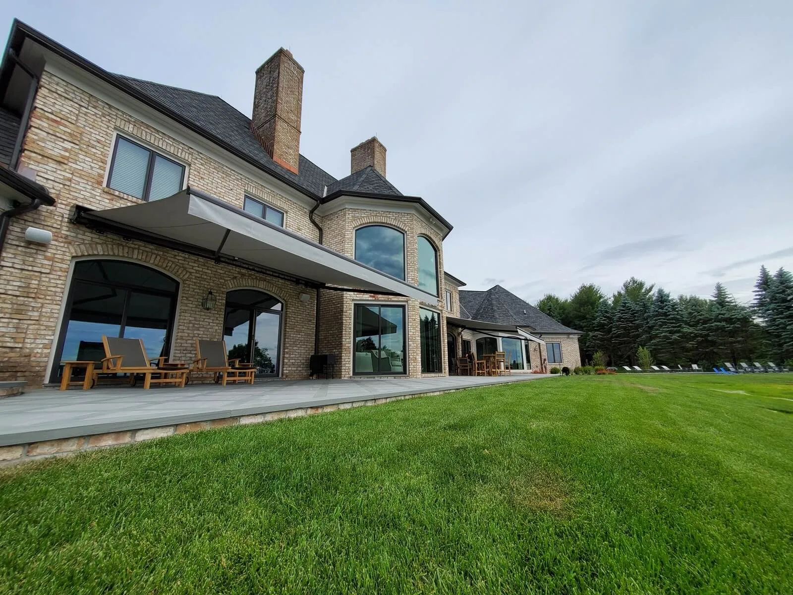 Large stone-and-brick home with a gray retractable awning deployed over a patio