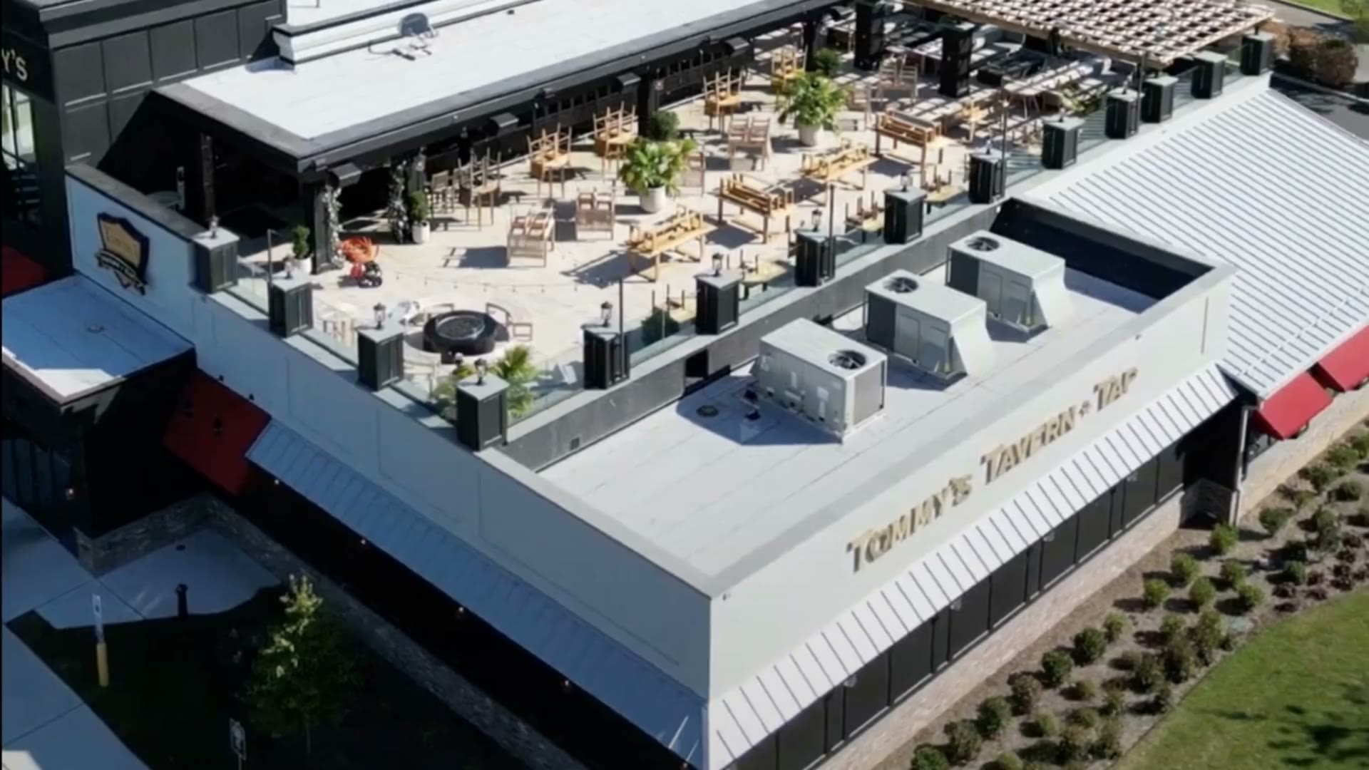 Aerial daytime photo of Tommy's Tavern + Tap rooftop patio with dining tables, chairs, planters, and rooftop HVAC units.
