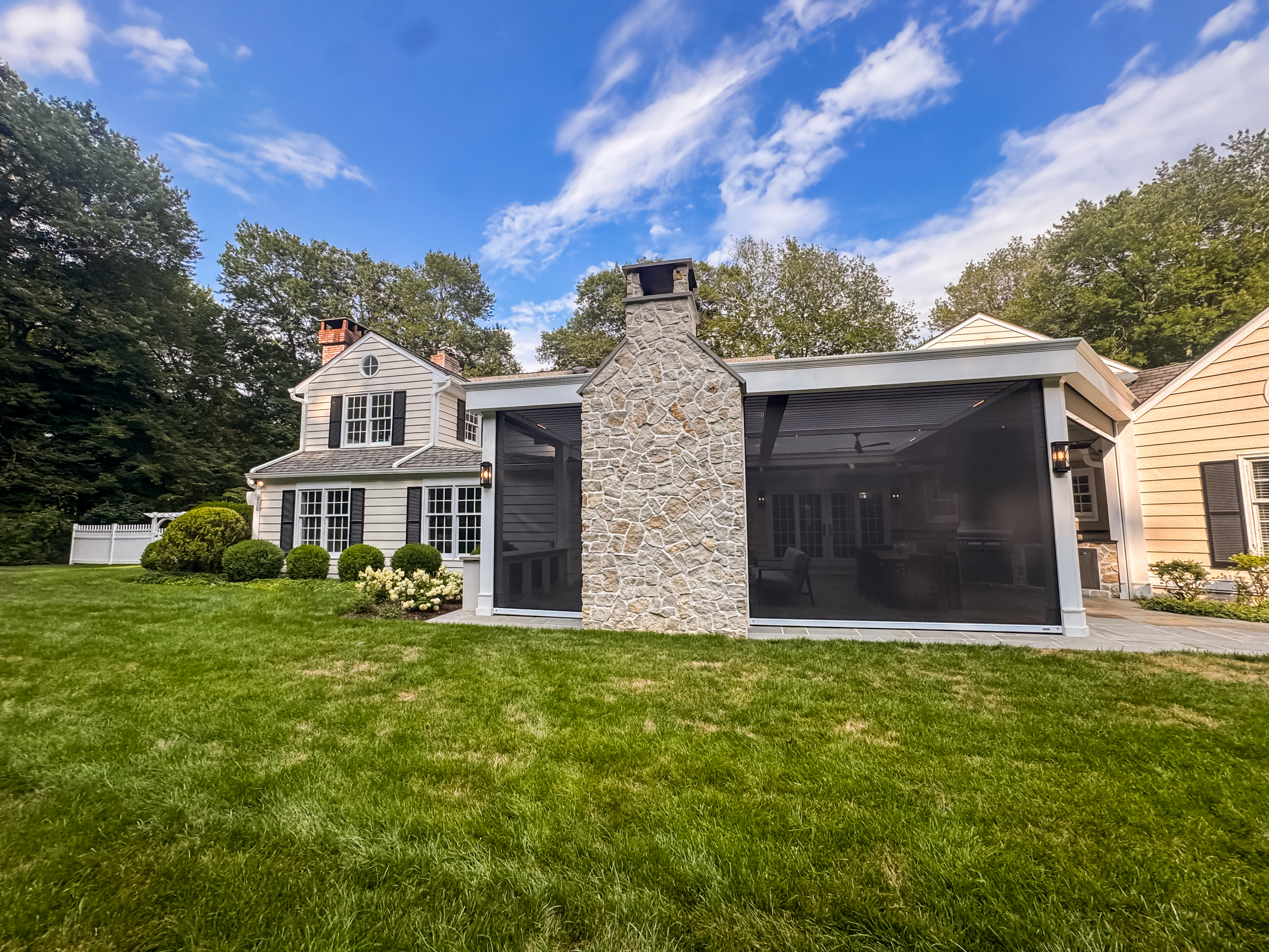 Hambrook project — full exterior view of completed outdoor room with louvered roof, stone fireplace, and motorized screens