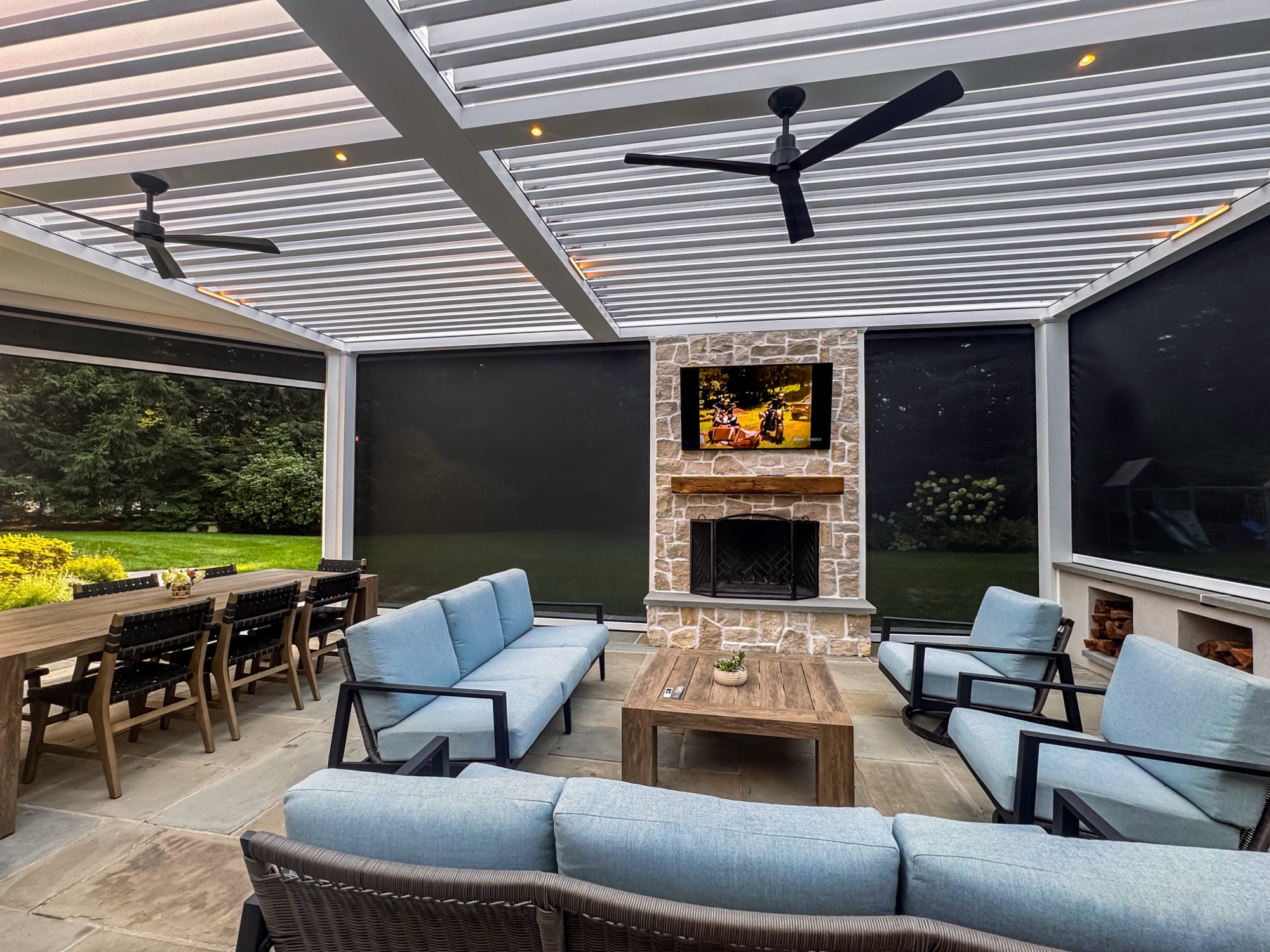 Interior of finished Hambrook outdoor room with stone fireplace, TV, lounge seating, and deployed screens
