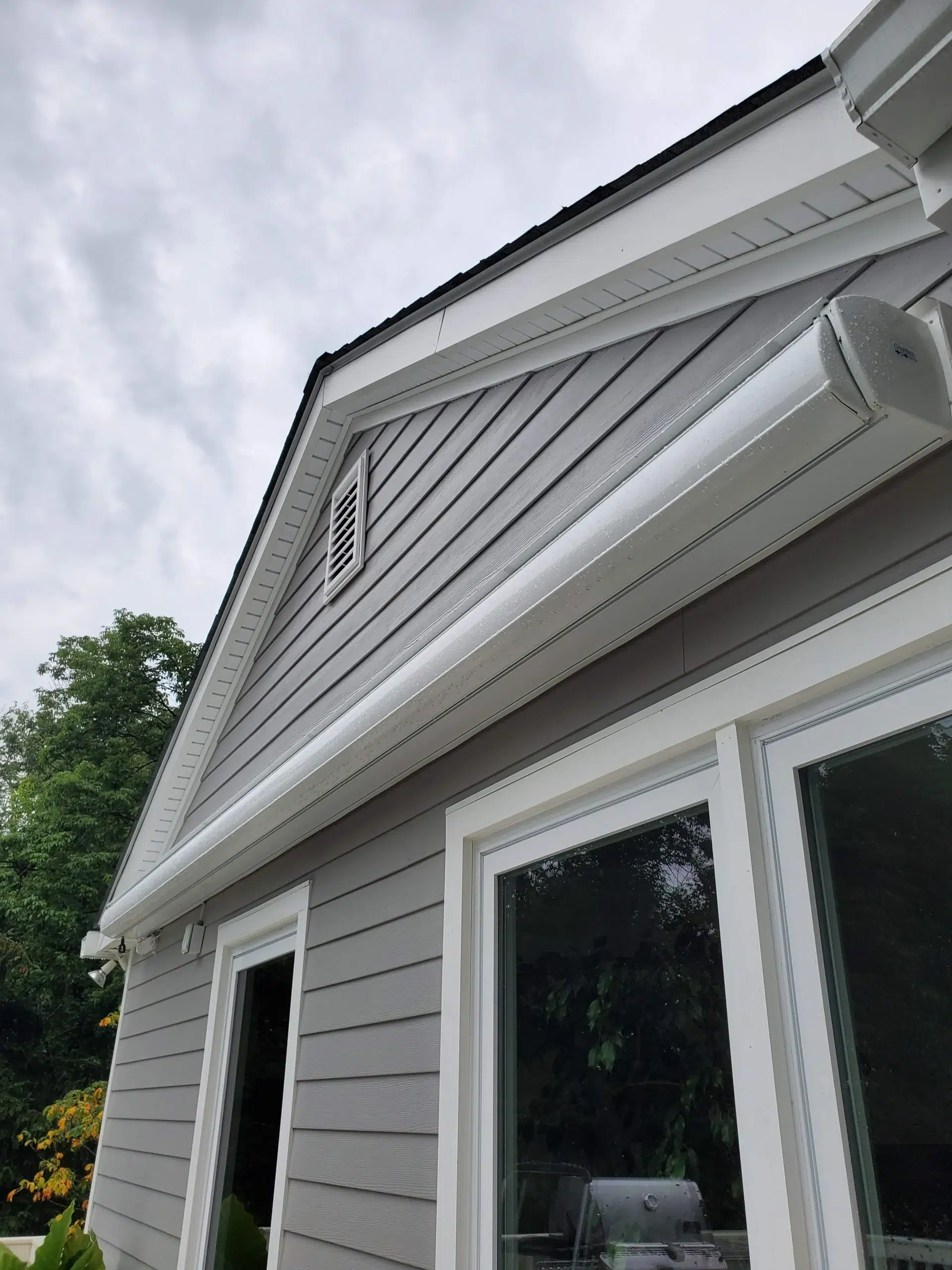 Closed retractable awning cassette mounted above large windows on a gray home exterior with a gabled roof.