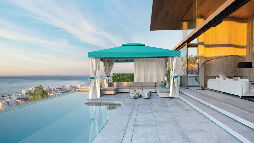 A luxurious poolside cabana with a teal canopy, white curtains, and modern lounge seating overlooking the ocean, creating a serene and elegant outdoor retreat.