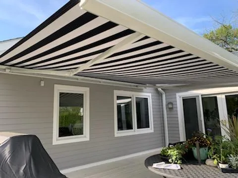 Black-and-white striped retractable awning extended over a backyard patio of a modern gray home with sliding glass doors.