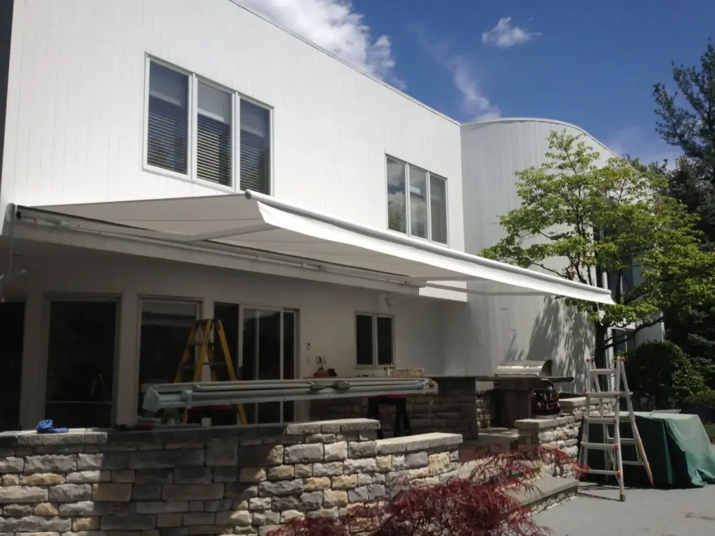 Retractable awning extended over a stone-trimmed patio area of a modern white home during installation.