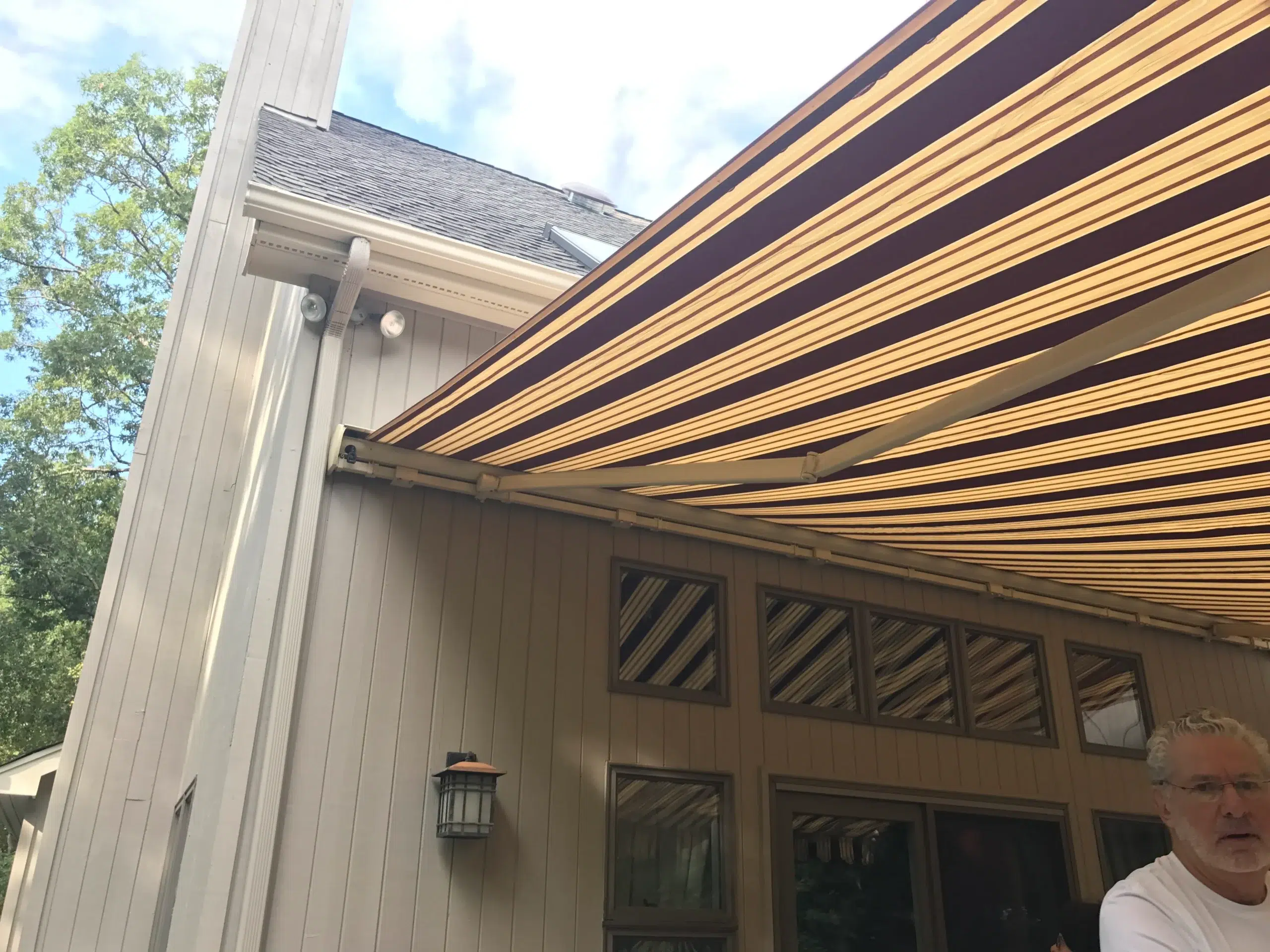 Close-up view of a striped retractable awning extended over a home’s patio entrance with windows and exterior lighting.