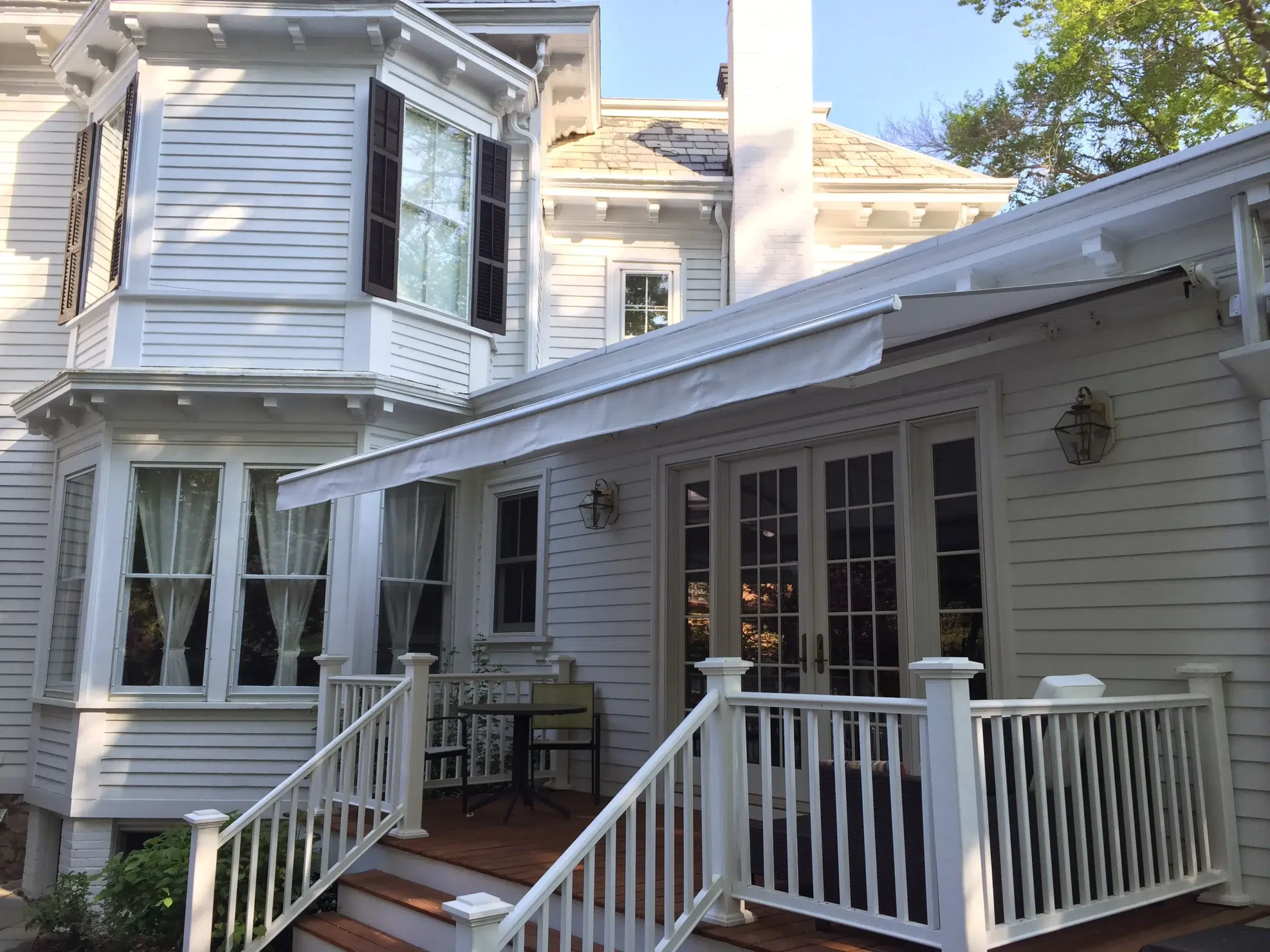 Retractable awning extended over a raised porch featuring French doors, white railings, and a classic-style home exterior.