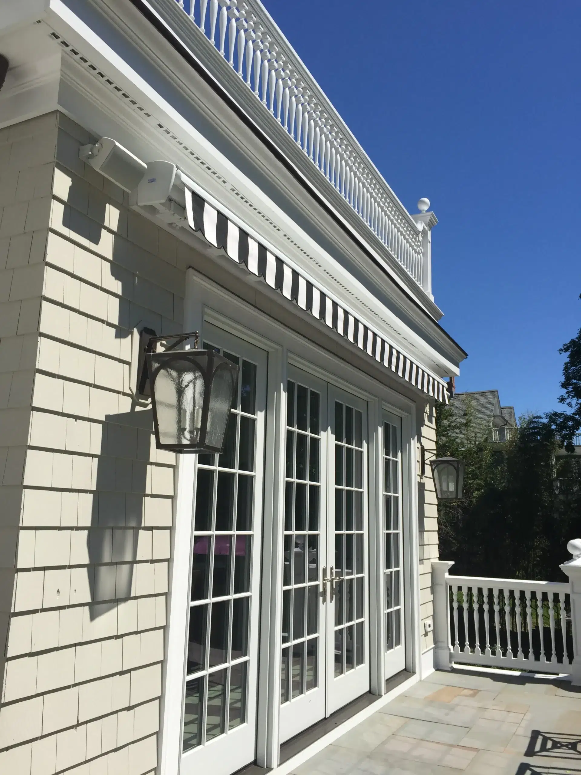Black-and-white striped retractable awning installed above large French doors on a light-colored home exterior under a clear blue sky.