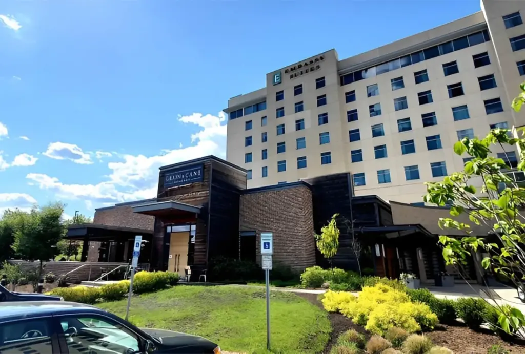 Exterior view of a modern hotel with a multi-story building, landscaped grounds, and a welcoming entrance under a blue sky.