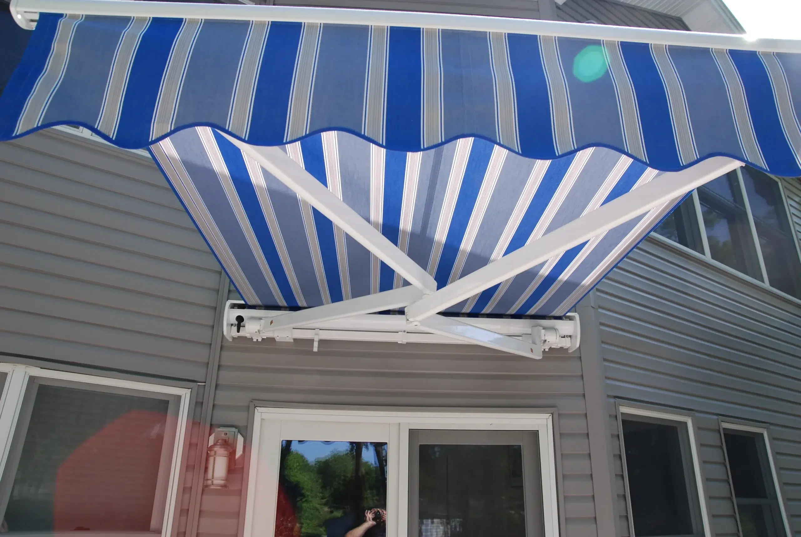 Close-up view of a blue-and-white striped retractable awning extended over a patio door on a gray home exterior.
