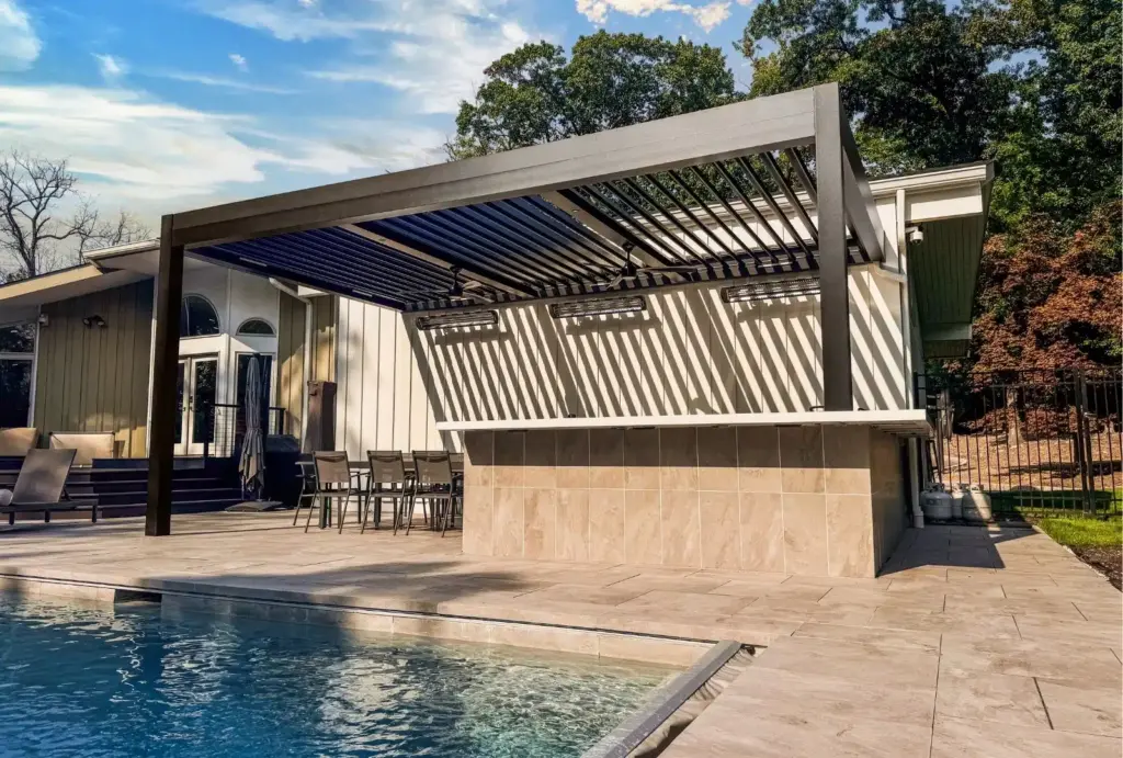 A sleek modern louvered pergola providing shade over a poolside patio with outdoor seating, attached to a residential backyard.