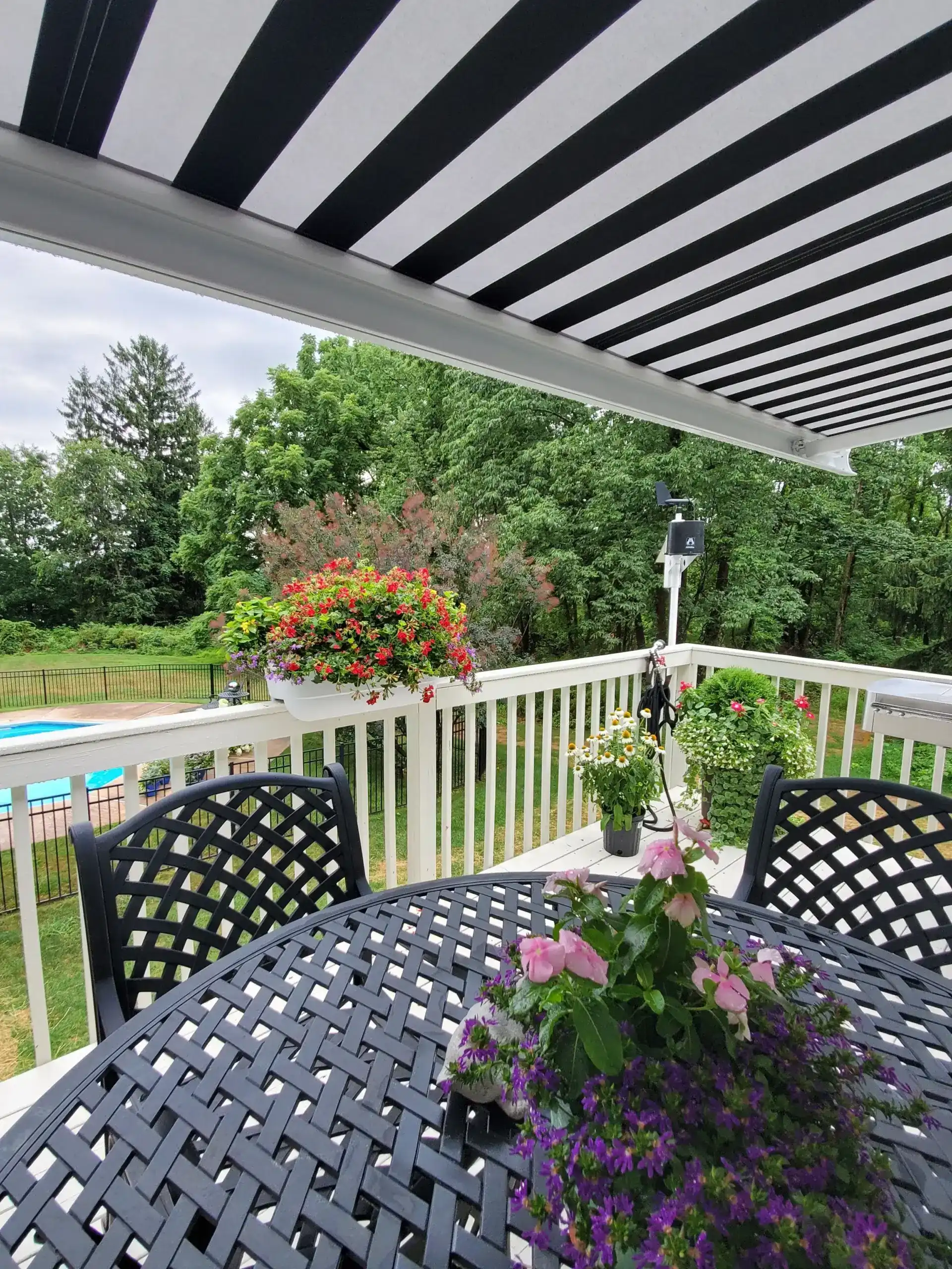 Black-and-white striped retractable awning providing shade over an outdoor deck with a metal dining table, flowers, and a garden view.