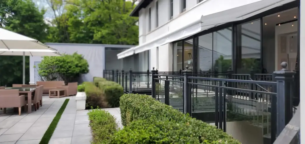 A sleek retractable awning extending over a patio dining area, with modern furniture and greenery surrounding the outdoor space.