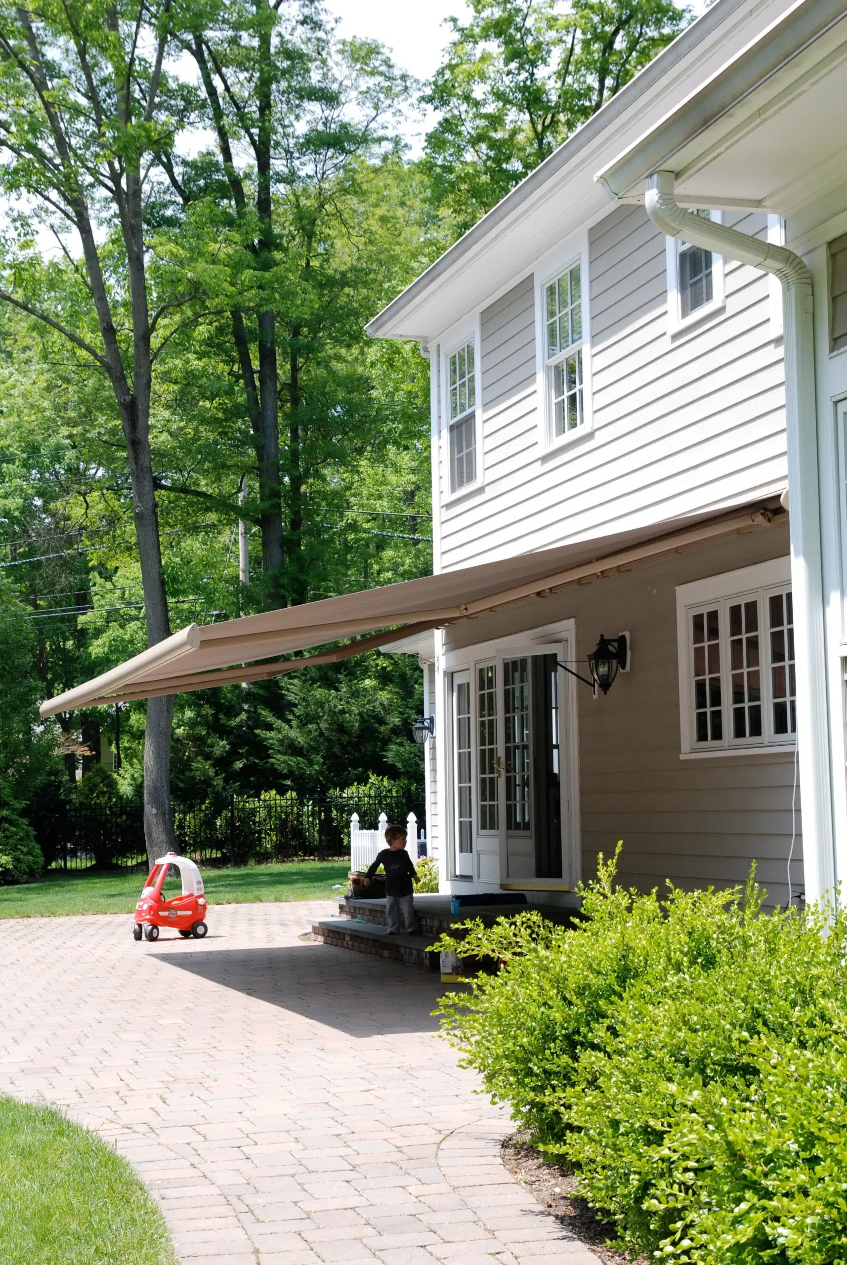 Retractable awning providing shade to a patio area of a residential home with lush greenery in the background.