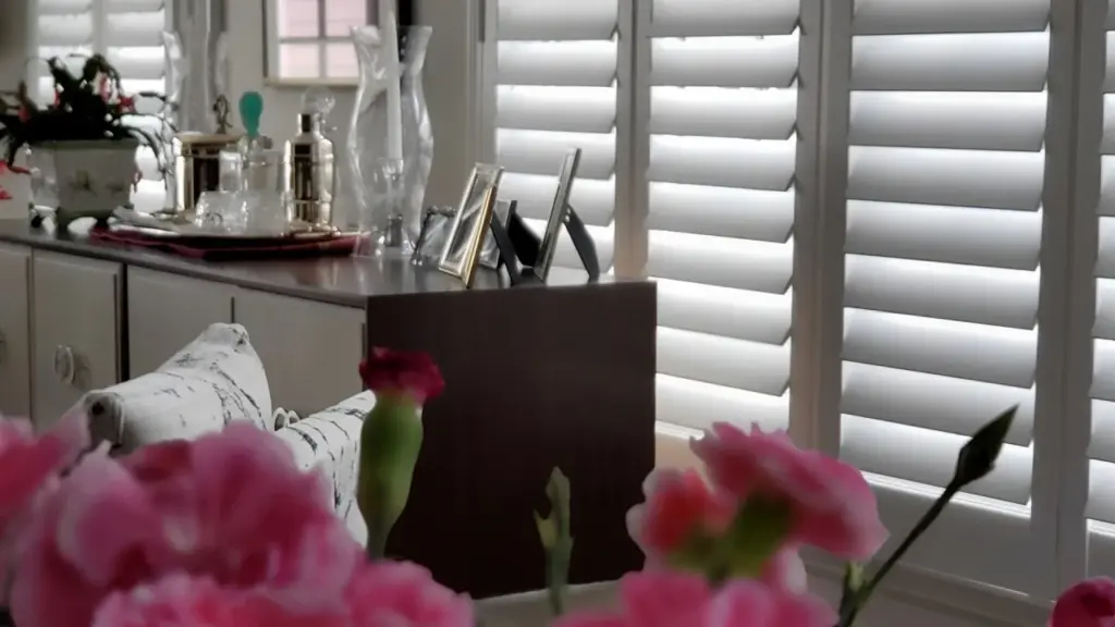 Close-up view of a bedroom dresser and décor with white plantation shutters filtering natural light in the background.