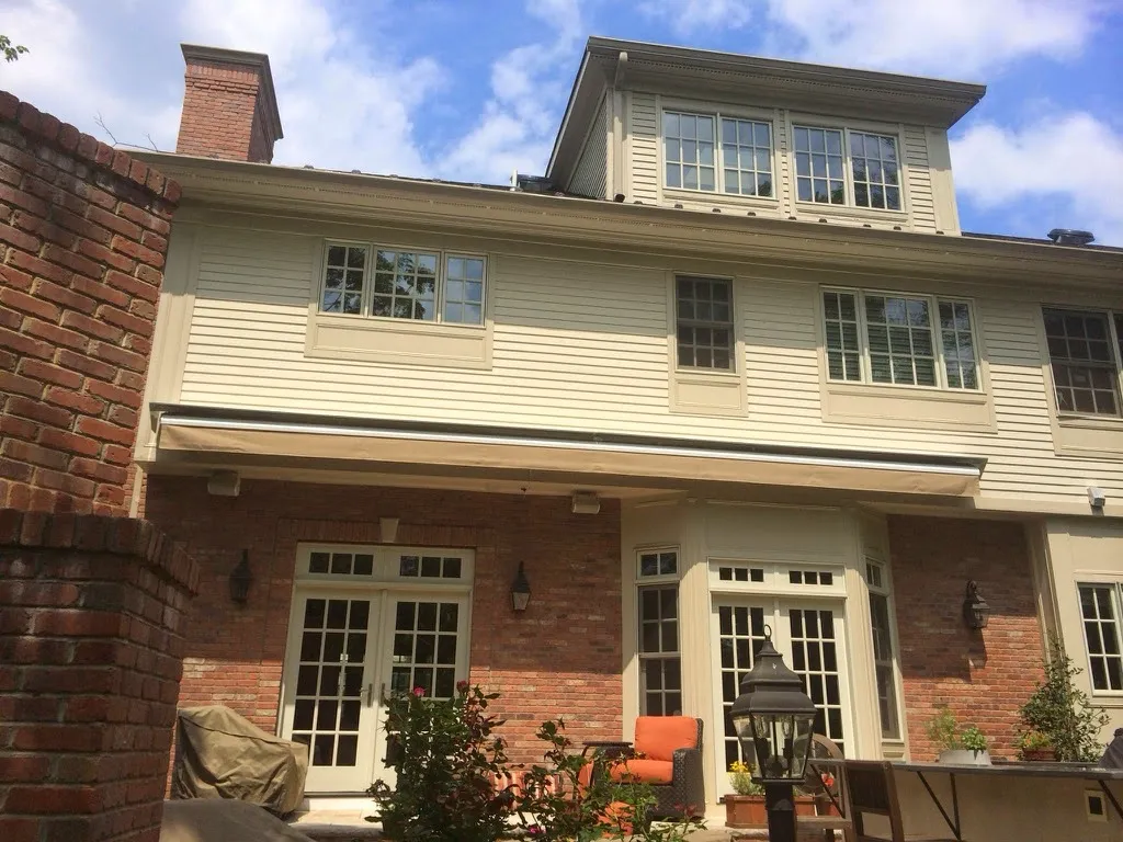 A retractable awning mounted above a brick patio entrance with outdoor chairs, enhancing shade and comfort for the backyard area.