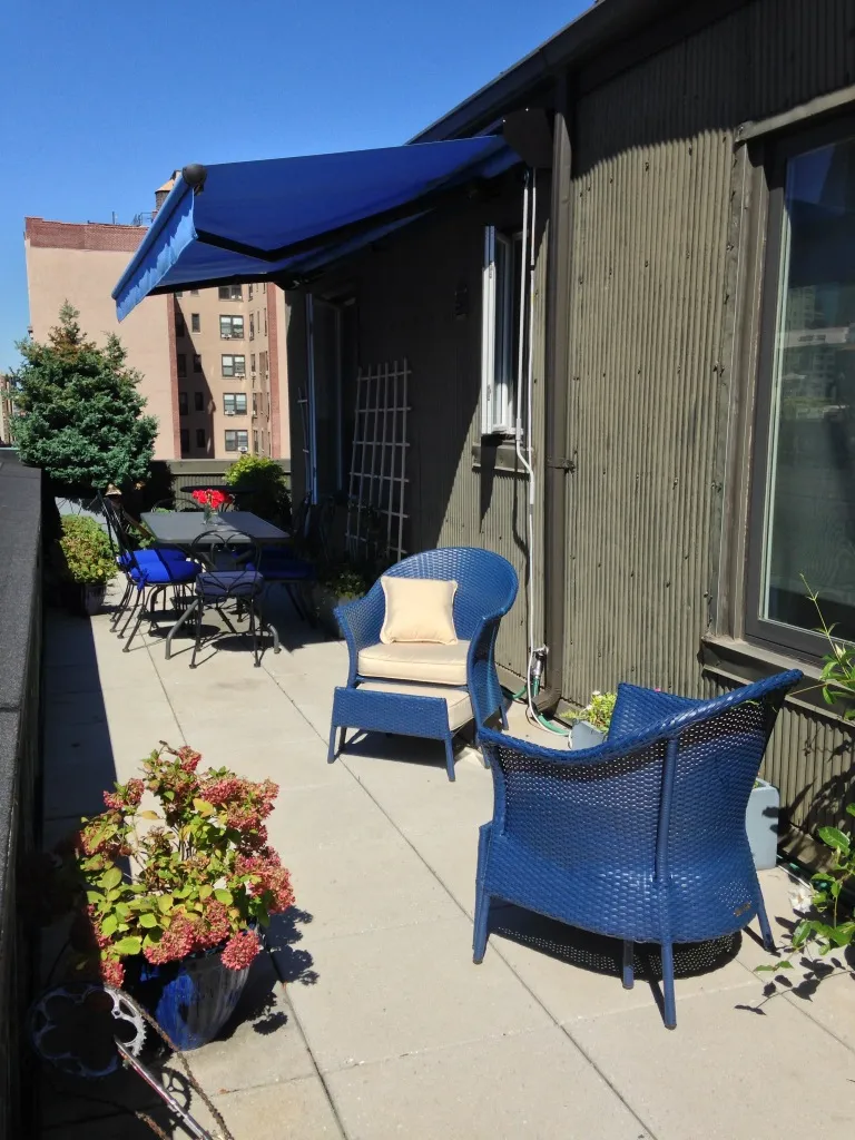 A modern blue retractable awning extending over a rooftop or balcony patio with stylish blue chairs and potted plants.