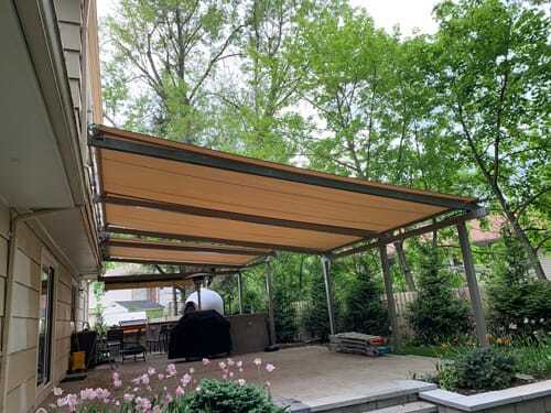 Retractable patio awning extended over a backyard seating area with lush greenery and garden landscaping.