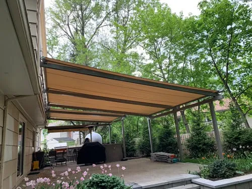 Retractable patio awning extended over a backyard seating area surrounded by greenery and garden plants.