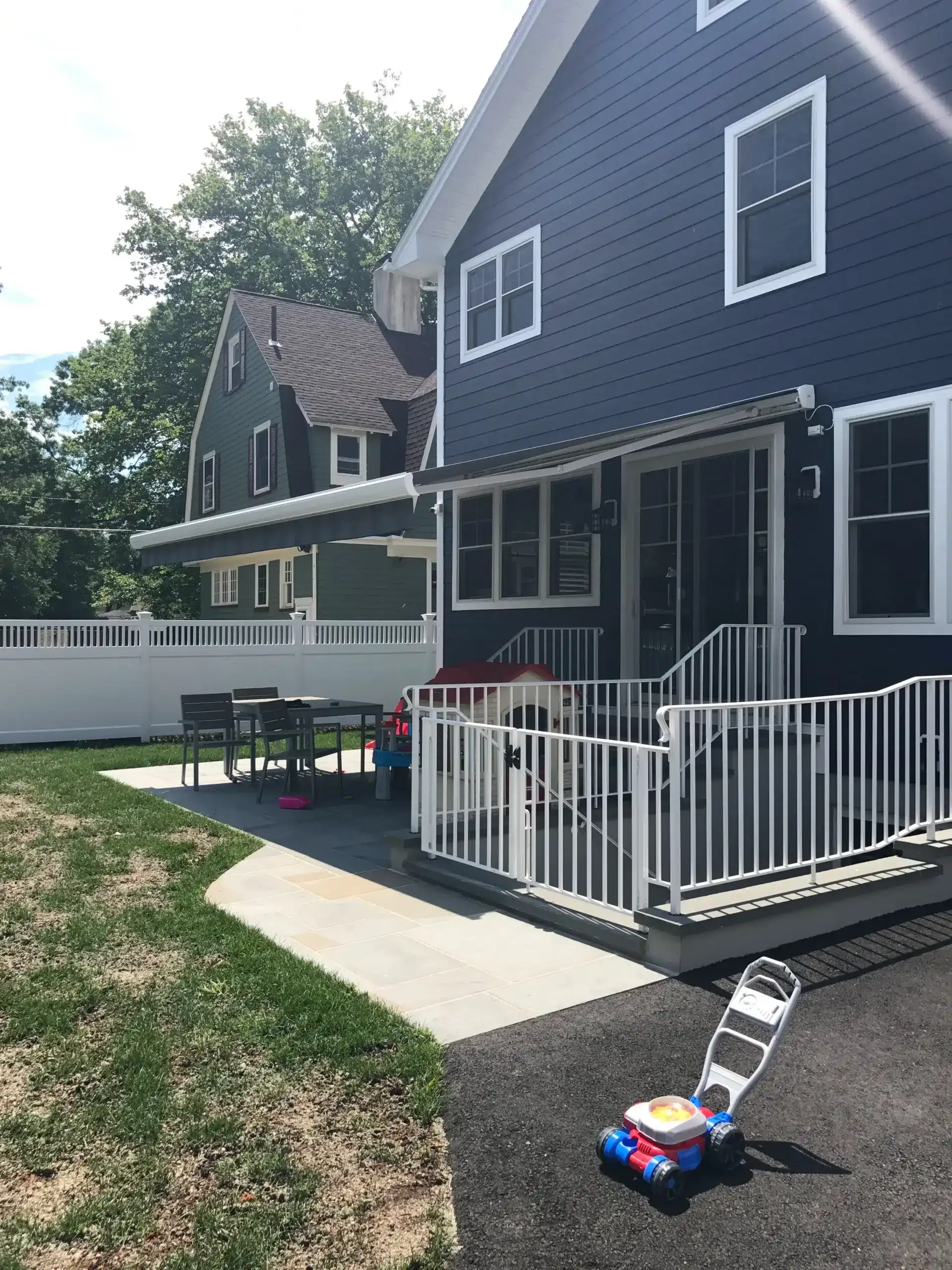 Retractable awning extended over a backyard patio attached to a dark-colored home with a fenced yard and outdoor seating.