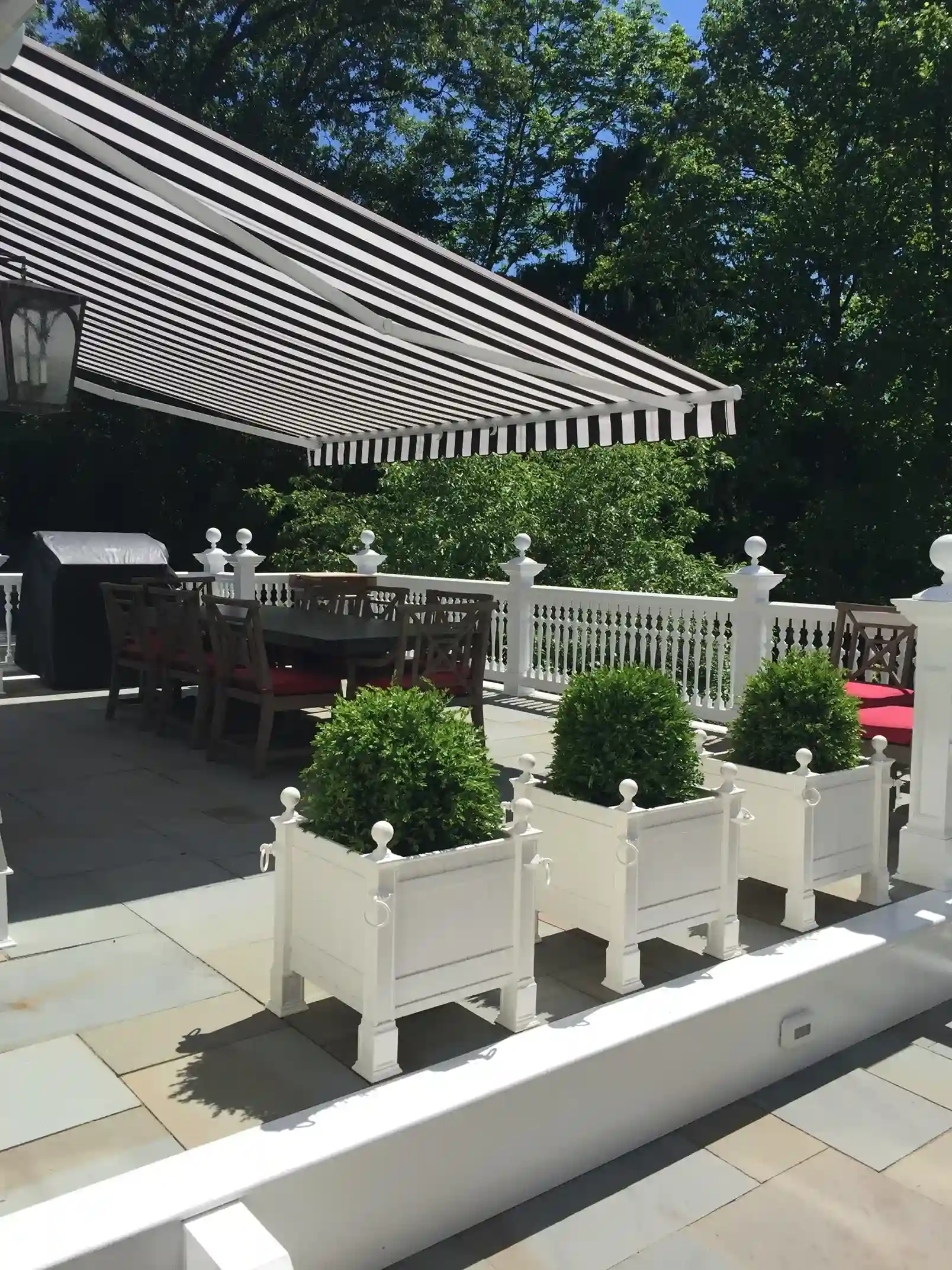 Black-and-white striped retractable awning shading a patio with white planters, outdoor seating, and garden views.