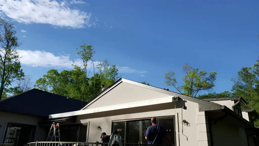 Technicians installing a retractable awning on a residential patio under a clear blue sky.