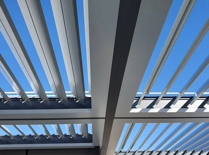 Close-up view of a modern motorized louvered roof with open aluminum slats against a clear blue sky.