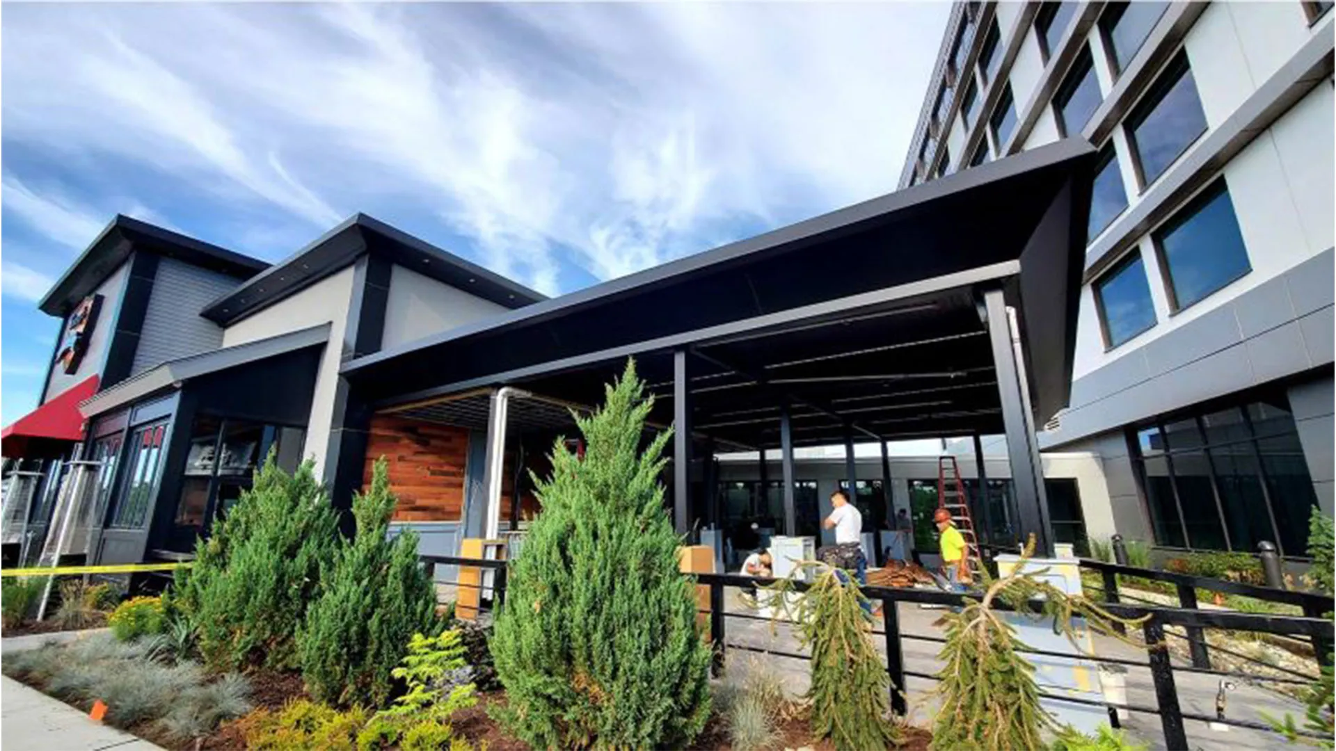 Large black motorized pergola installed at a commercial property, featuring outdoor seating and landscaped greenery.